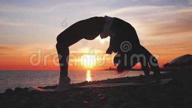 <strong>剪影</strong>年轻女子在海上日落时练习瑜伽。 快乐的生活时刻-海滩上的<strong>剪影</strong>瑜伽